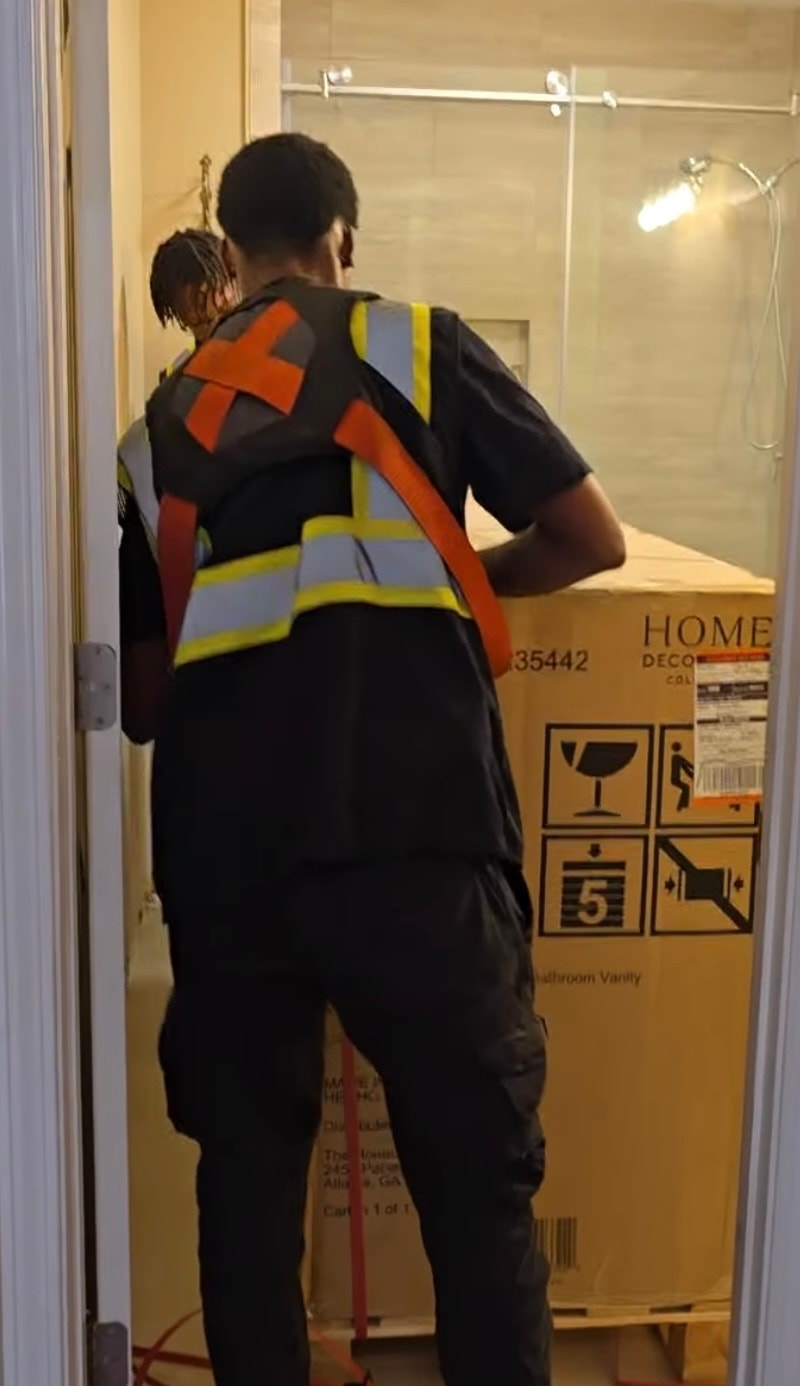 TTC crew in safety vests maneuvering a large boxed vanity through a bathroom doorway
