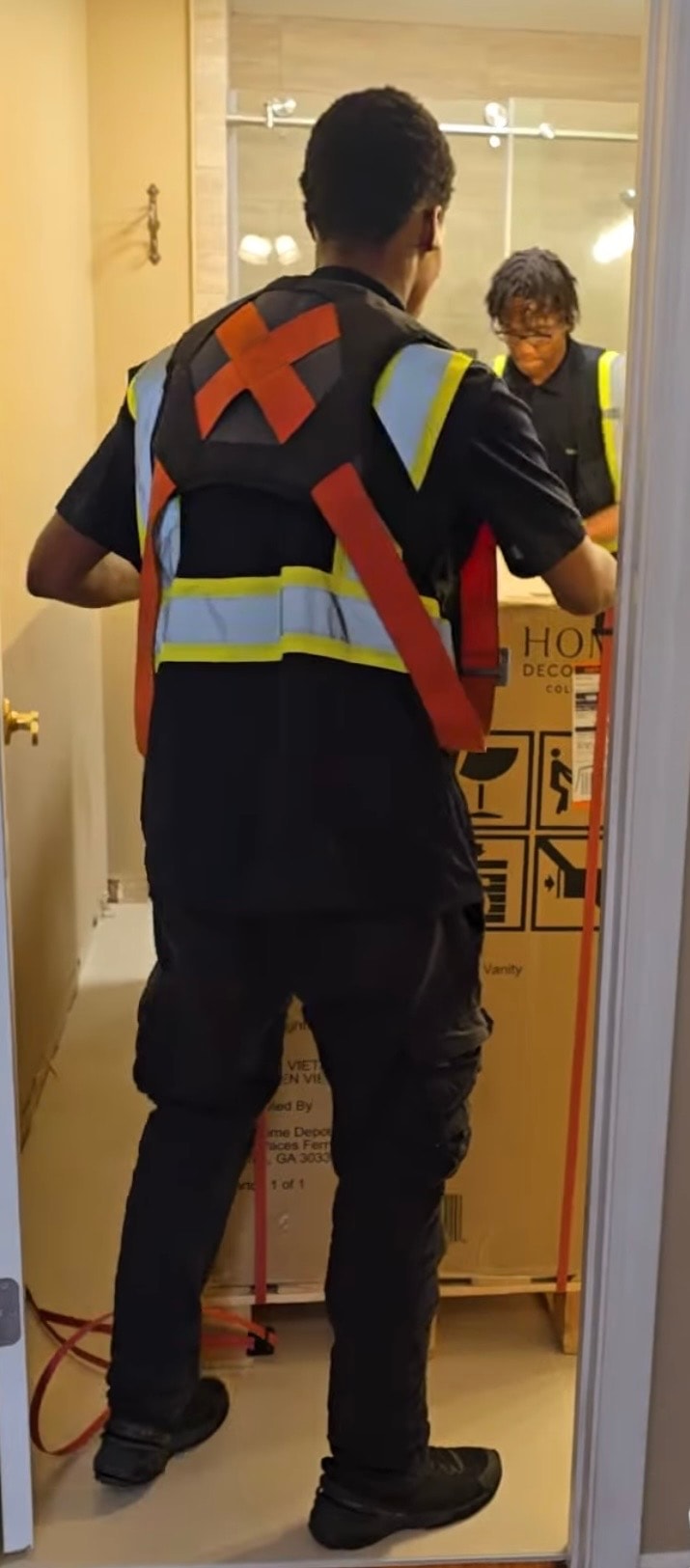Two TTC crew members in safety vests positioning a boxed vanity in a bathroom